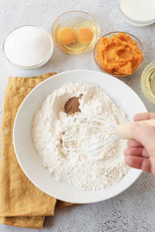 Flour, spices, and baking ingredients for pumpkin bread on a light countertop.