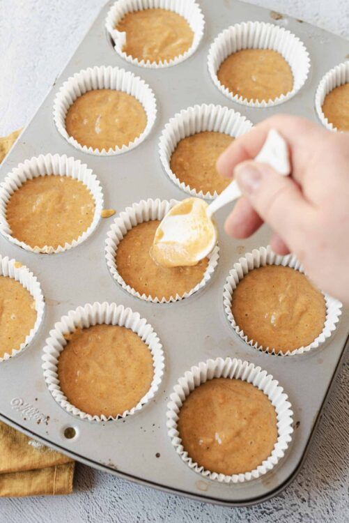 Cream cheese frosting being added to freshly baked cupcakes in a muffin tin.