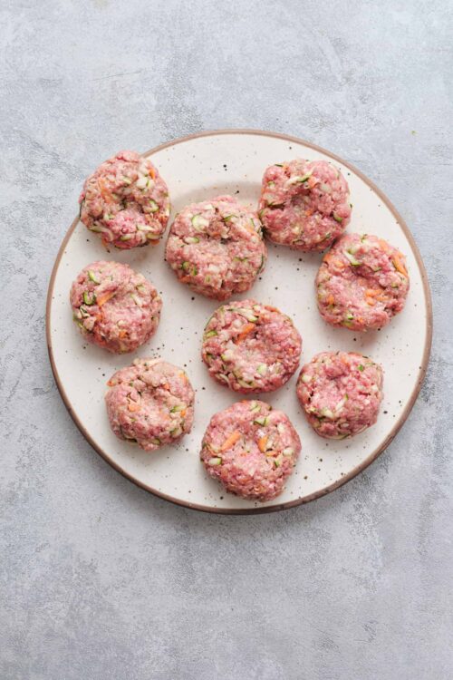 Minced meat mixture with vegetables for meatballs on white plate.