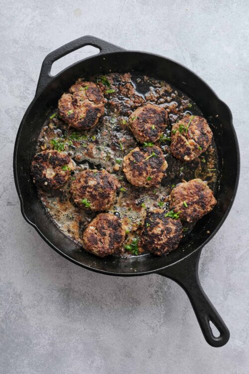 Savory beef meatballs in cast iron skillet with herbs and juices.