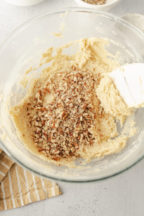 Creamy cookie dough with chopped nuts in a glass mixing bowl, ready for baking.