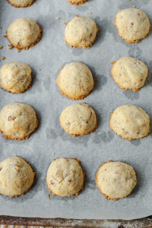 Buttery cookie dough balls with chopped nuts on baking sheet.