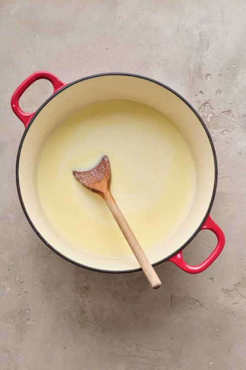 Creamy melted butter in a yellow enameled cast iron saucepan with a wooden spoon.