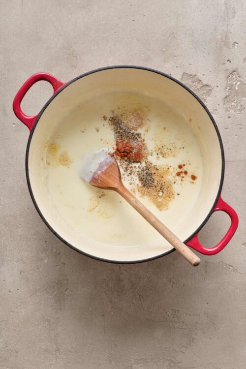 Rich creamy sauce with spices and seasonings in a red Dutch oven for baking bread.