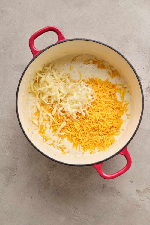 Cheddar cheese and shredded cheese in a creamy cheese sauce in a red cast iron skillet, ready for baked cheese recipes.