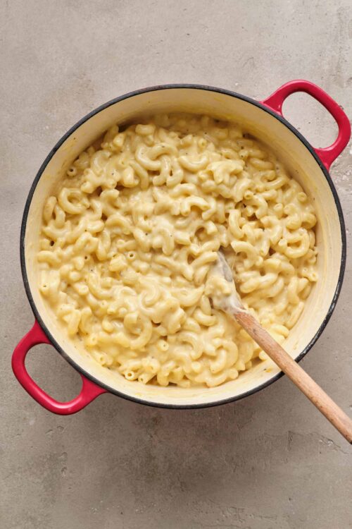 Creamy macaroni and cheese in a red enameled cast iron pot.