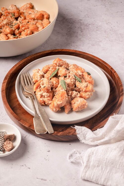 Creamy sweet potato gnocchi with sage and Parmesan on a white plate.