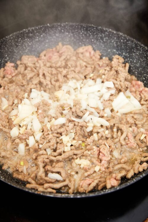 Ground beef and chopped onions cooking in a skillet, perfect for savory recipes.