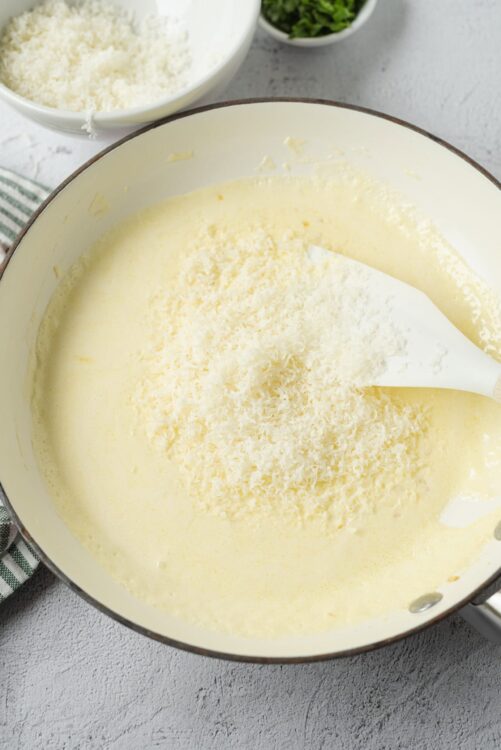 Creamy cheese sauce in a skillet with grated cheese on top for homemade mac and cheese recipe.