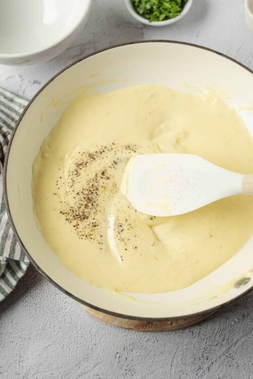 Creamy homemade cheese sauce melting in a skillet with black pepper, ideal for pasta or nachos.