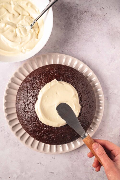 Rich chocolate cake with vanilla frosting being spread on top.