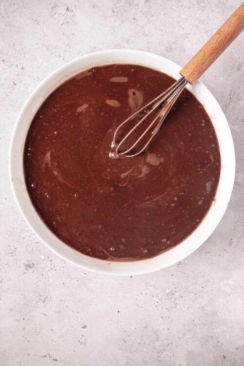 Rich chocolate batter for homemade baked goods with a whisk in a white bowl.
