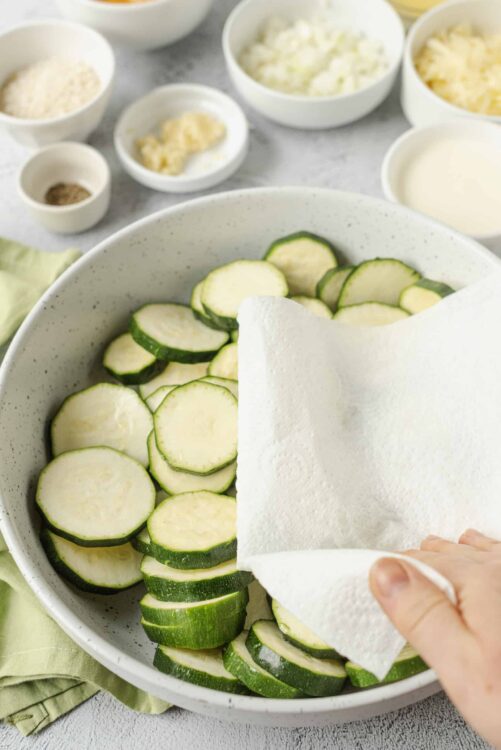 Fresh zucchini slices in a white bowl with paper towel drying.