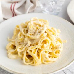 Creamy fettuccine alfredo on a white plate with black pepper garnish, served with a cozy dining setup.