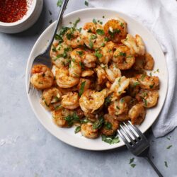 Juicy garlic butter shrimp garnished with fresh herbs on a white plate.