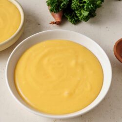 Creamy lemon soup with fresh herbs on a white surface.