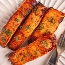 Grilled salmon fillets with fresh herbs on a white plate, healthy seafood dinner.