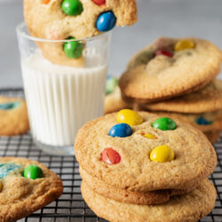Colorful sugar cookies with M&M's on cooling rack and glass of milk.