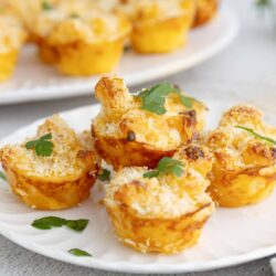 Golden baked cheesy potato cups with crispy bread crumb topping on white plate, fresh parsley garnish.