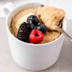 Fresh berry cobbler served in a white mug, topped with vanilla ice cream and ripe berries.