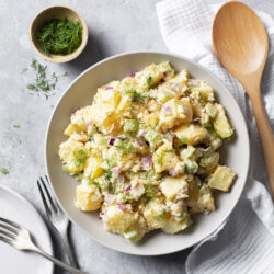 Creamy potato salad with herbs, egg, celery, and red onion, topped with fresh dill.