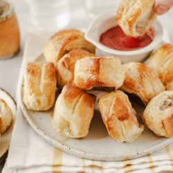 Flaky sausage rolls with dipping sauce on a white plate.