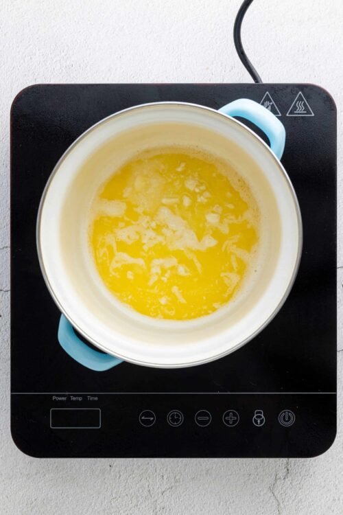 Butter melting in a white saucepan on an electric stove.