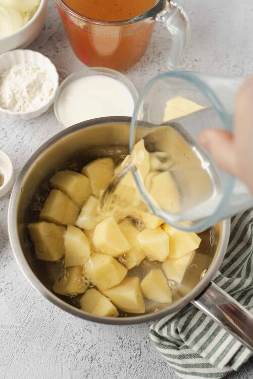 Creamy potato soup being prepared with milk and broth, surrounded by baking ingredients and kitchen tools.