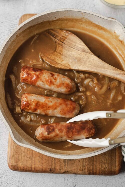 Savory sausage and onion gravy in a Dutch oven with wooden spoon and tongs.