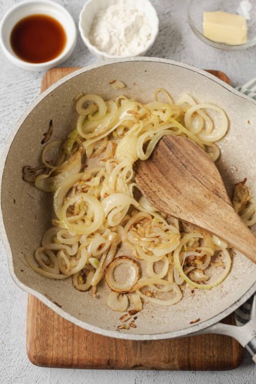 Sautéed onions in a skillet with wooden spoon, ready for recipe preparation.