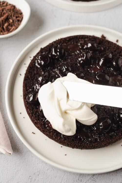 Decadent chocolate cherry cake with whipped cream frosting on a white plate. Perfect for dessert lovers and special occasions.