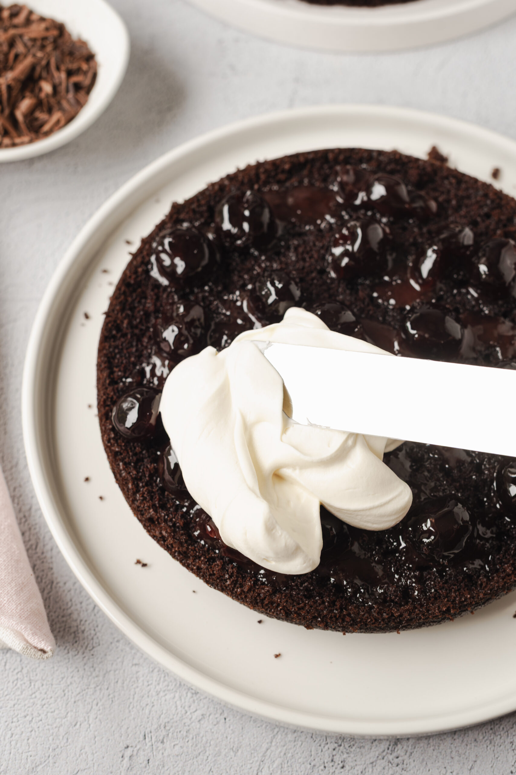 Decadent chocolate cherry cake with whipped cream frosting on a white plate. Perfect for dessert lovers and special occasions.