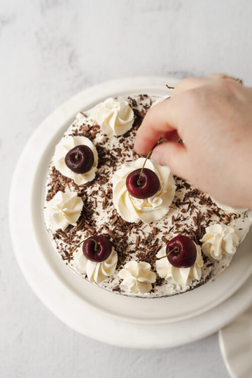 Fresh cherry-topped layered chocolate cake with whipped cream and chocolate shavings.