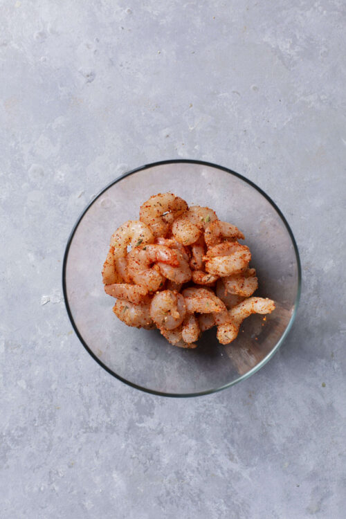 Raw shrimp coated with seasoning in a glass bowl for cooking or recipes.