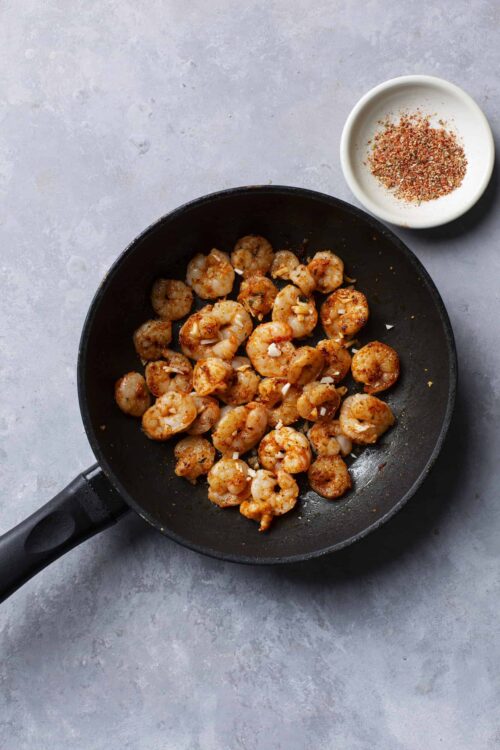 Juicy sauteed shrimp in a black skillet with garlic and seasoning on a gray surface.