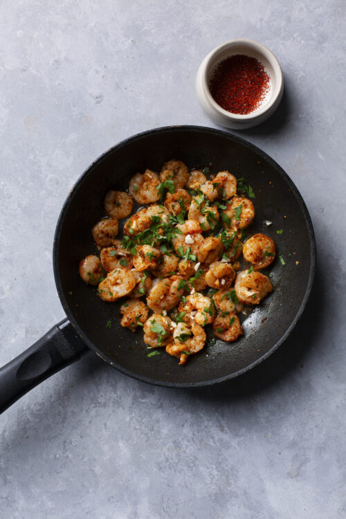 Juicy shrimp sautéed with spices and fresh parsley in a black skillet.