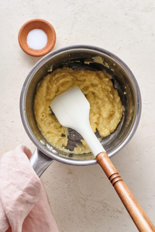 Creamy mashed potatoes being stirred in a stainless steel pot with a white spatula.