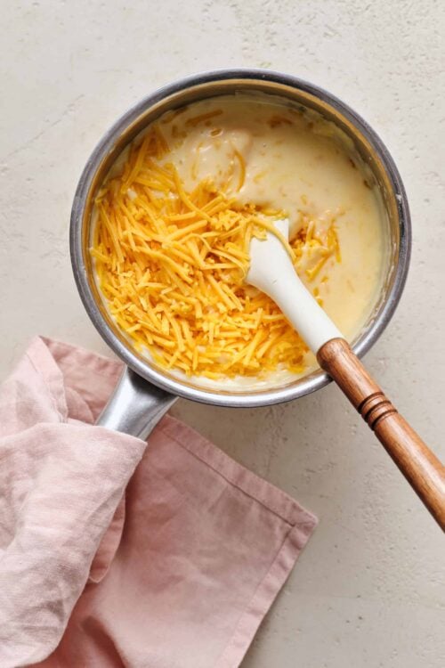 Creamy cheese sauce with shredded cheddar cheese in a saucepan.