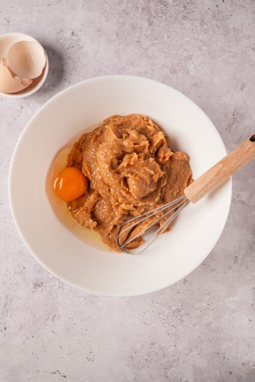 Creamy cookie dough with egg yolk and a whisk in a white bowl, ready for baking.