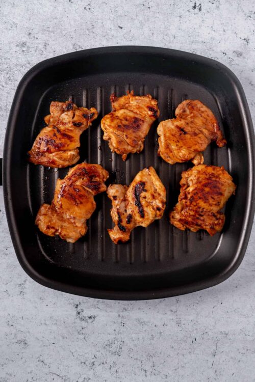 Grilled chicken thighs on a black stovetop grill pan, cooked to perfection with grill marks.