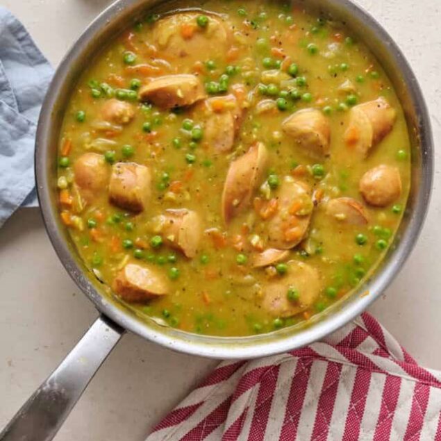 Creamy chicken and vegetable soup in a stainless steel pan with peas and carrots.