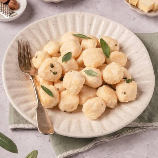 Creamy cauliflower gnocchi served on a textured beige plate, garnished with sage leaves. Perfect for healthy comfort food recipes.