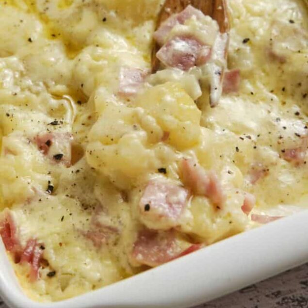Creamy potato ham casserole baked dish with melted cheese, crispy bacon, and black pepper, perfect for comfort food.