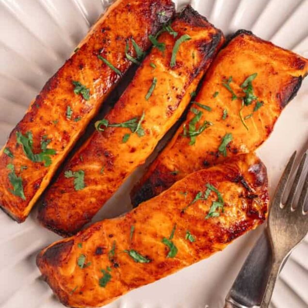 Grilled salmon with fresh herbs on a white plate, close-up.