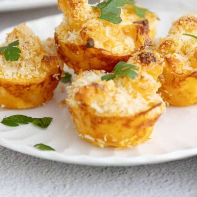 Golden baked cheesy potato cups with crispy bread crumb topping on white plate, fresh parsley garnish.