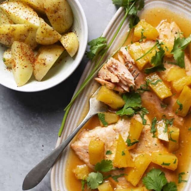 Crockpot salmon with pineapple and cilantro, served with roasted potatoes, on a light gray surface.