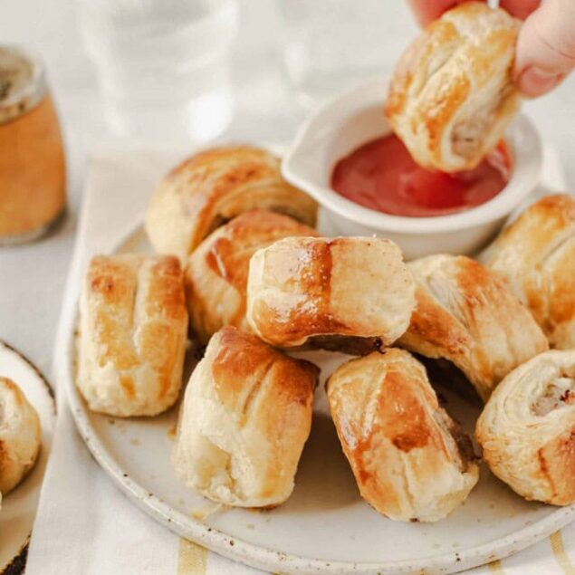Buttered sausage rolls with dipping ketchup on a white plate, perfect for snack or party.