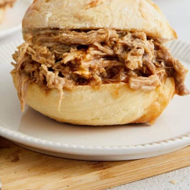 Savory BBQ pork sandwich on a soft, fluffy bun with pulled pork filling, served on a white plate.