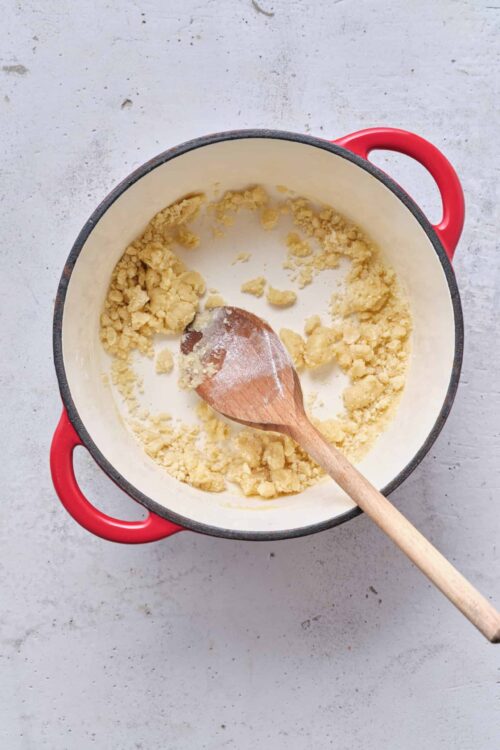 Crumbly pie crust dough in a red-handled enameled cast iron skillet with a wooden spoon.