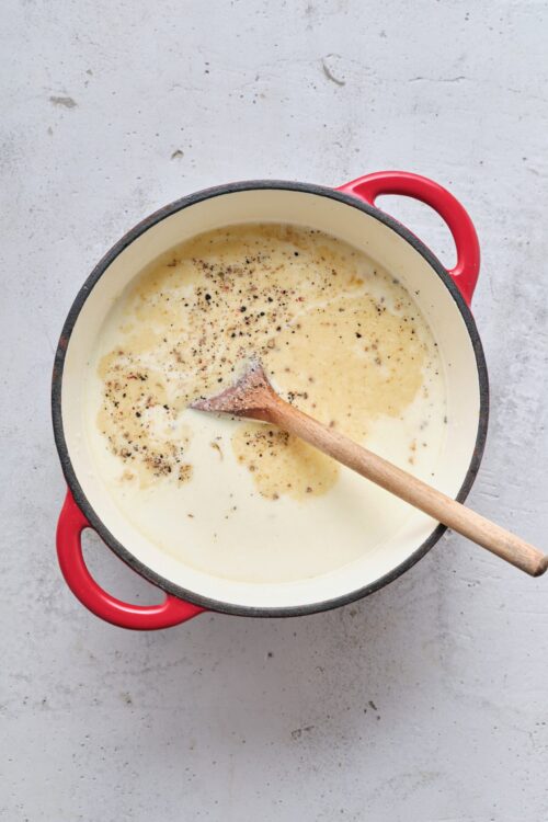 Creamy sauce with black pepper in a red-handled skillet.